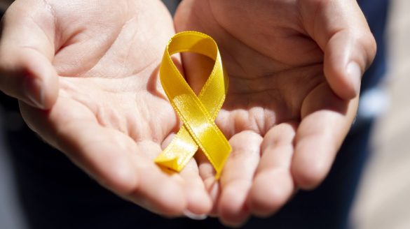 Close-up de mãos delicadamente segurando uma pequena fita amarela que representa a campanha do setembro amarelo