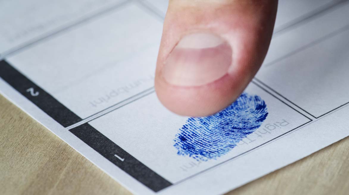 Close-up dedão de uma pessoa registrando a digital sobre uma folha com espaços demarcados.