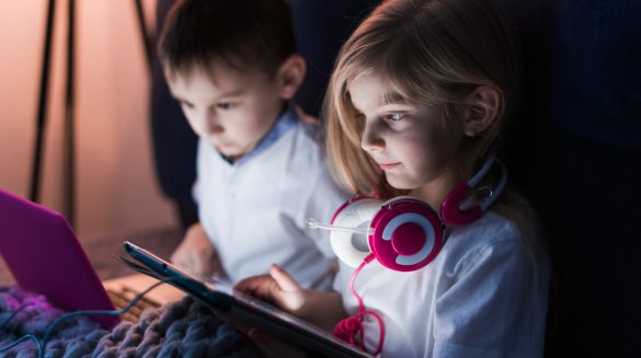 Um garoto com um notebook e uma garota com um tablet e um fone de ouvido gamer.
