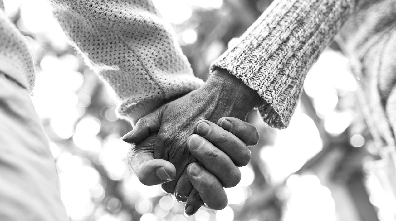 Close-up das mãos de um casal de idosos de mãos dadas.