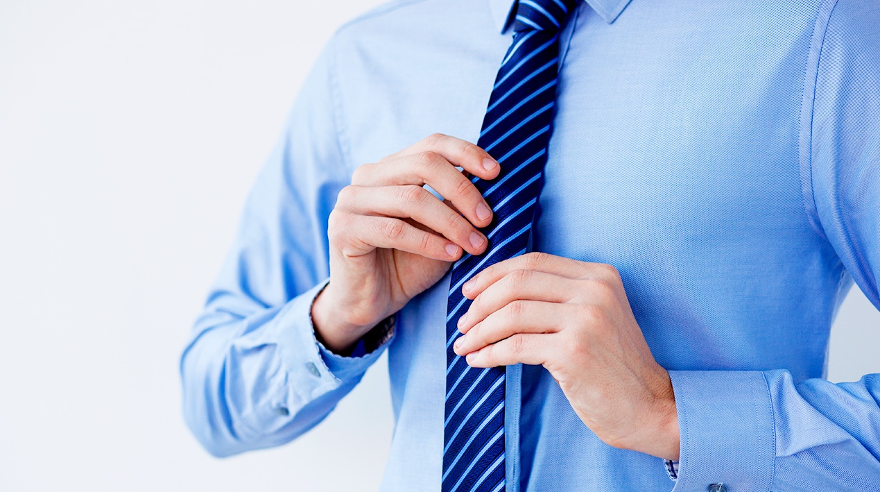 Homem com camisa social de manga longa ajustando a gravata.
