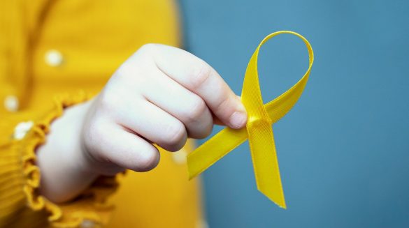 Mão infantil segurando uma fita amarela, a qual representa a campanha do maio amarelo, a qual visa chamar a atenção da sociedade para o alto índice de mortes no trânsito.