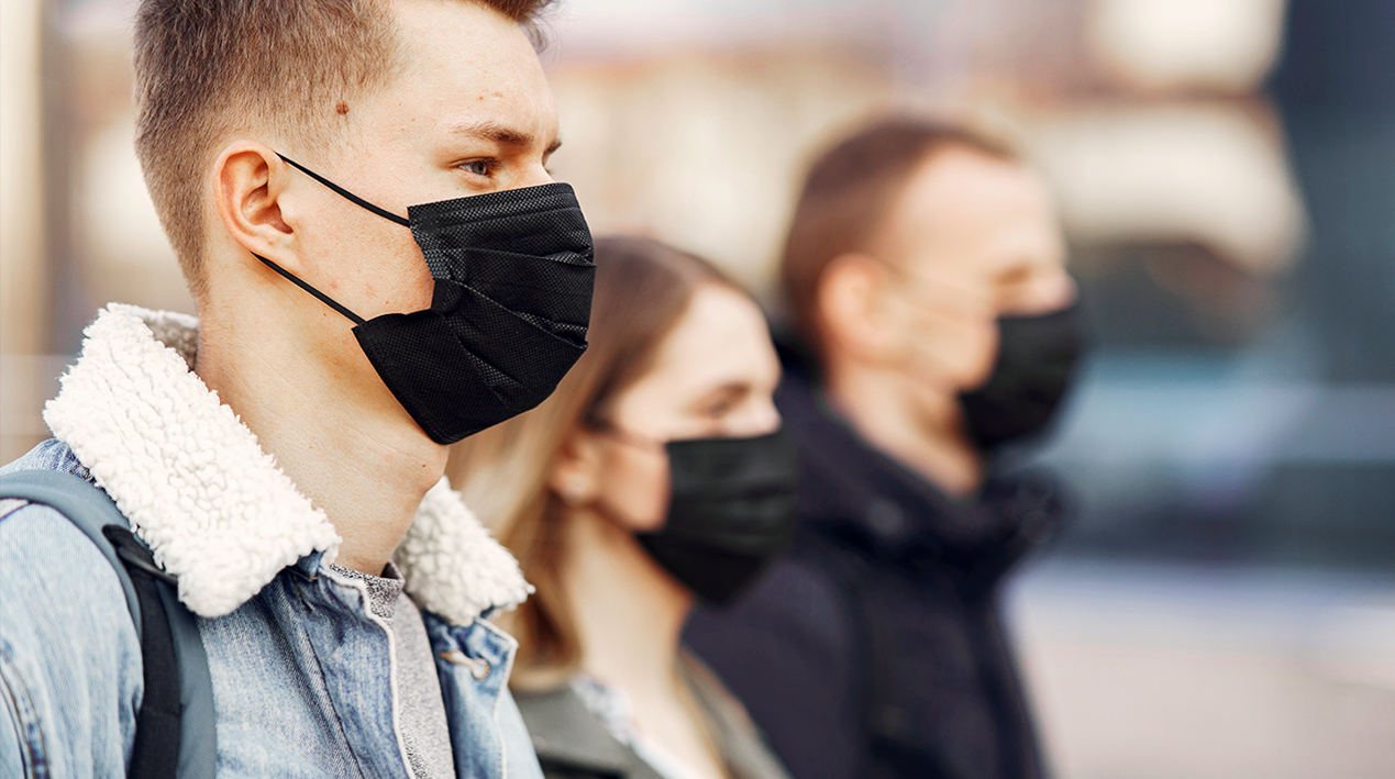 Três pessoas de perfil utilizando máscaras pretas para proteção contra a COVID-19.