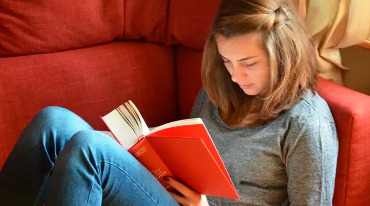 Garota sentada num sofá lendo um livro