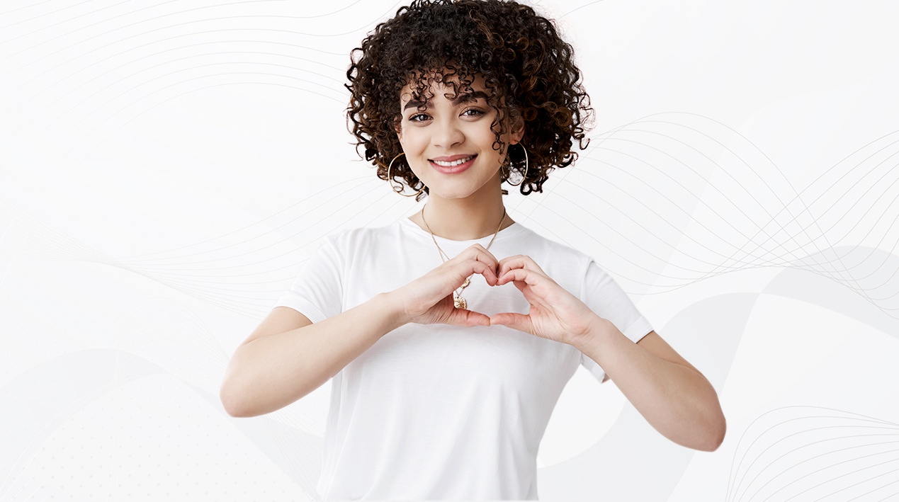 Imagem de uma mulher com as mãos unidas em formato de coração, na altura do peito, próximo ao coração.