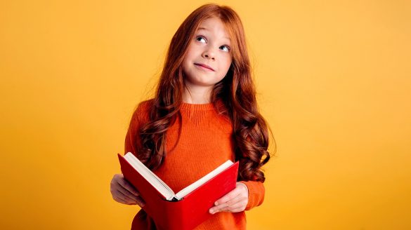 Garota de cabelos longos olhando para o alto e segurando nas mãos um caderno aberto.